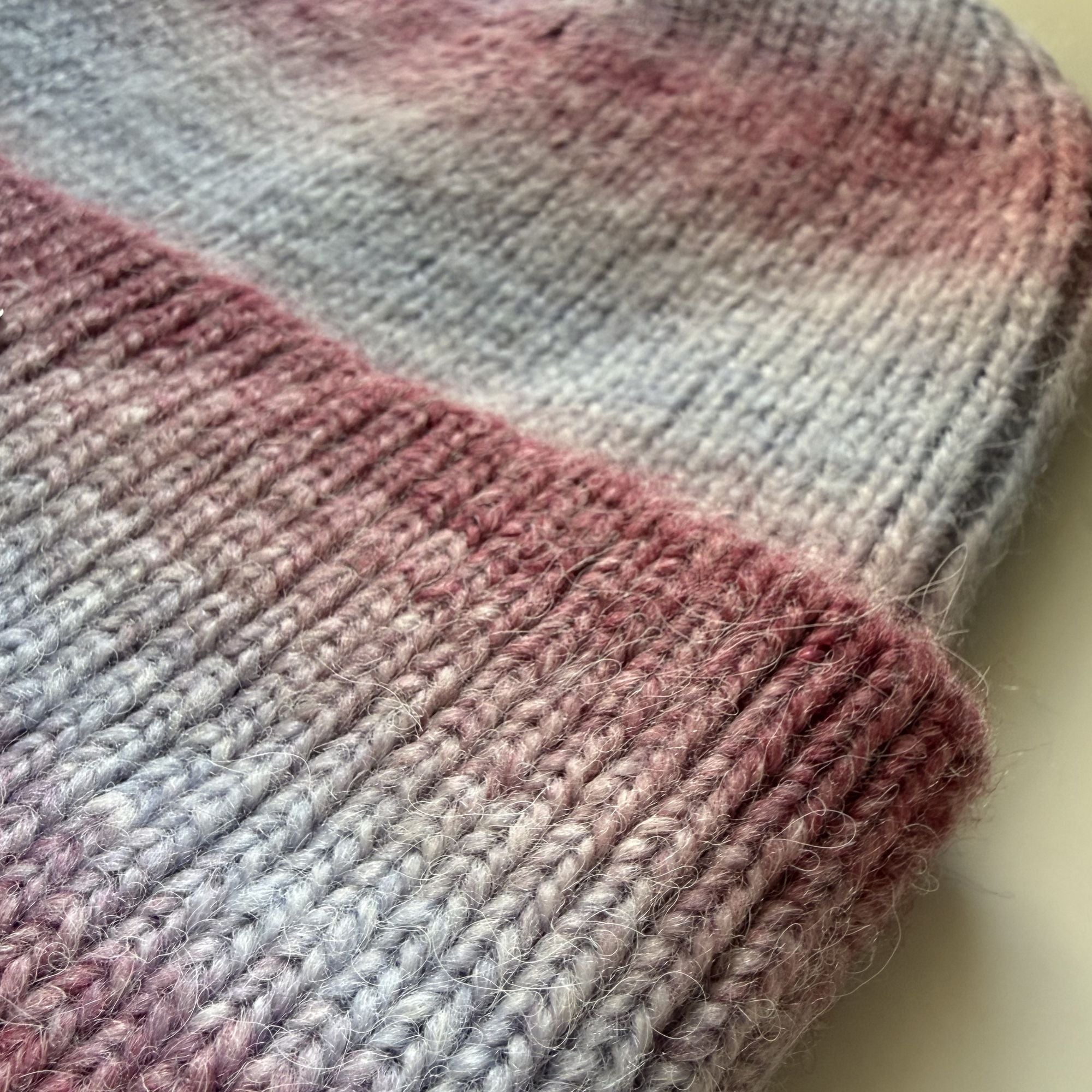 Close-up of a knitted fabric with pink and gray gradient on a light background