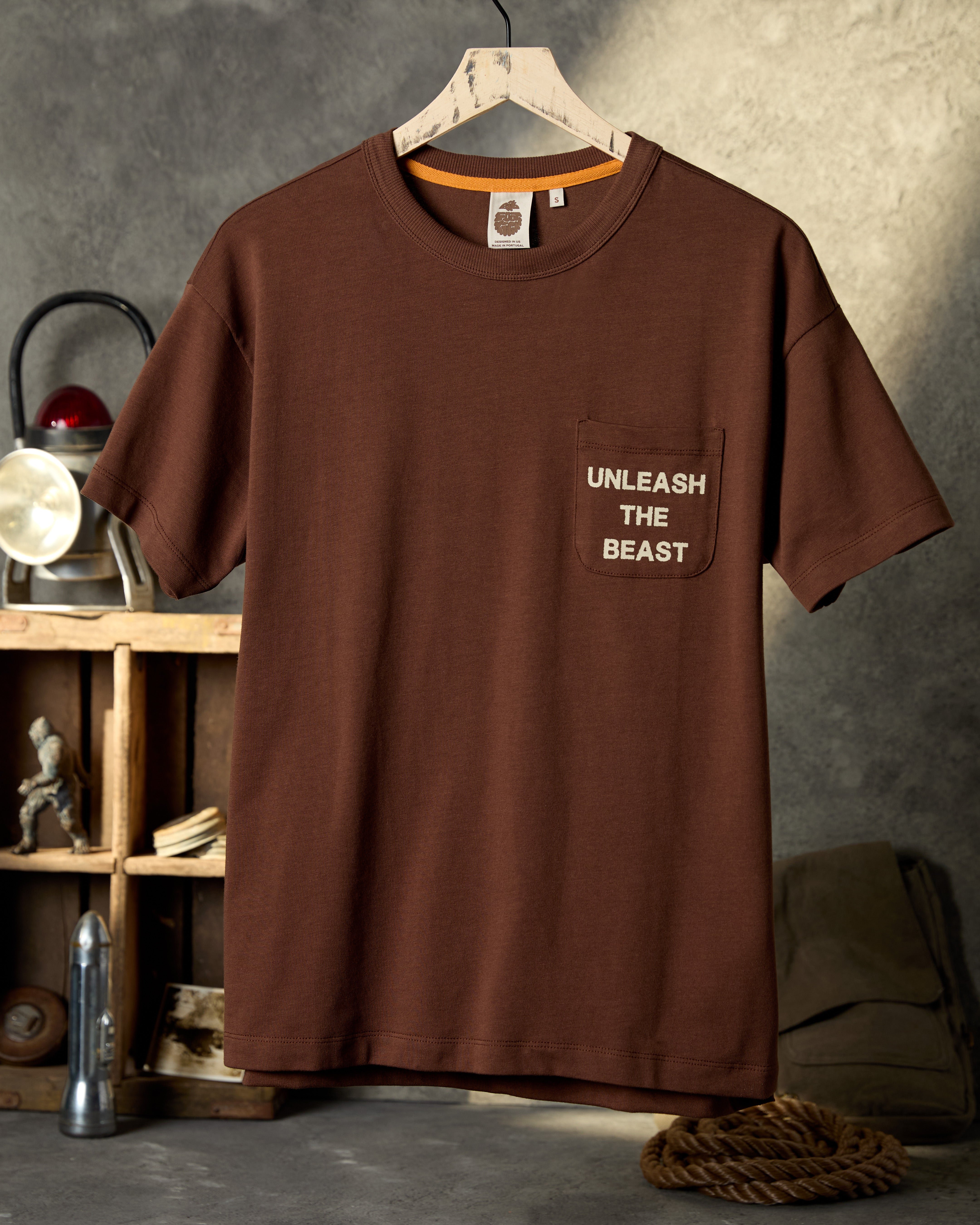 Brown t-shirt with 'Unleash the Beast' text on a hanger against a textured wall.