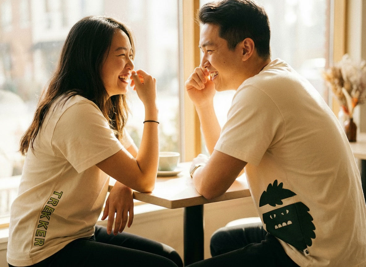 Two people sitting at a table in a bright room, smiling and laughing wearing Bigfoot Kick